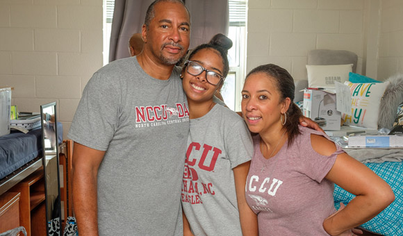 Picture of a happy mother and father helping their daughter un-pack her personal belonging at her dorm.