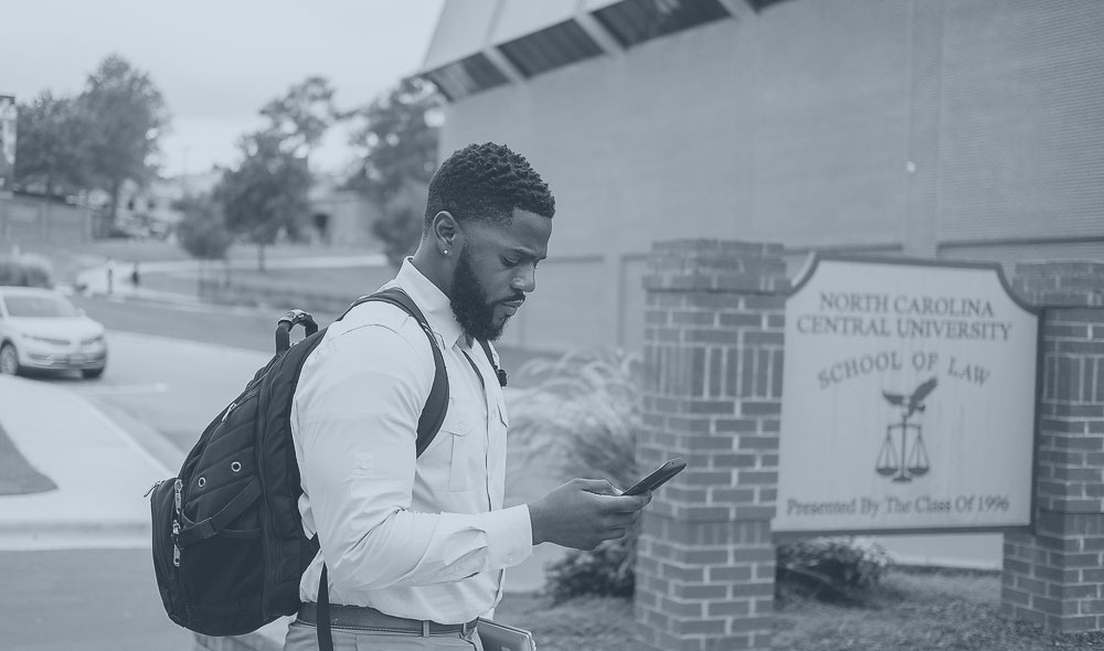 Law student in front of the law school, looking at his phone