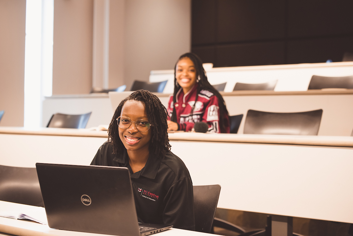 Two smiling students sitting in a lecture hall and looking towards the camera
