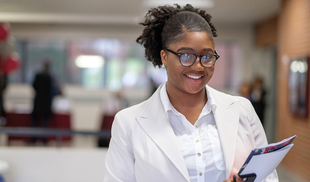 Student with glasses in all white attire, holding folders