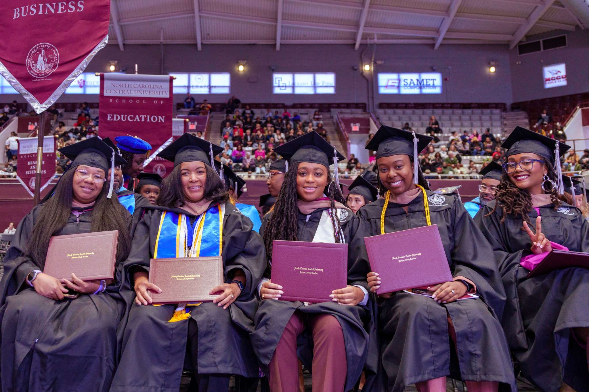 Graduates in caps and gowns holding diplomas, smiling at a ceremony.