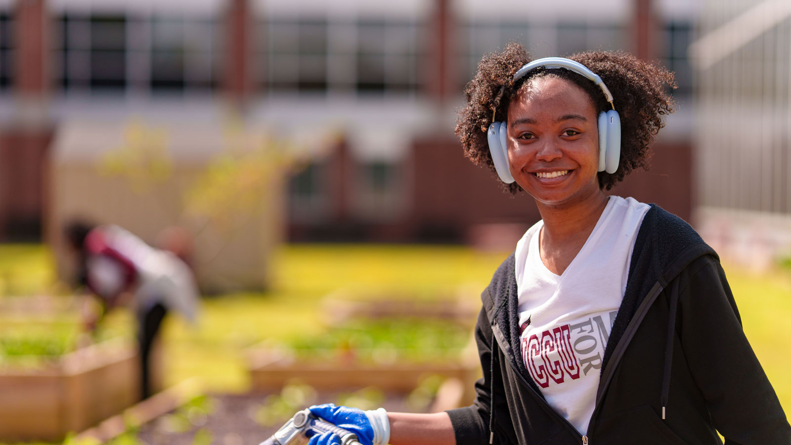 An NCCU student with headphones and gloves works in a garden