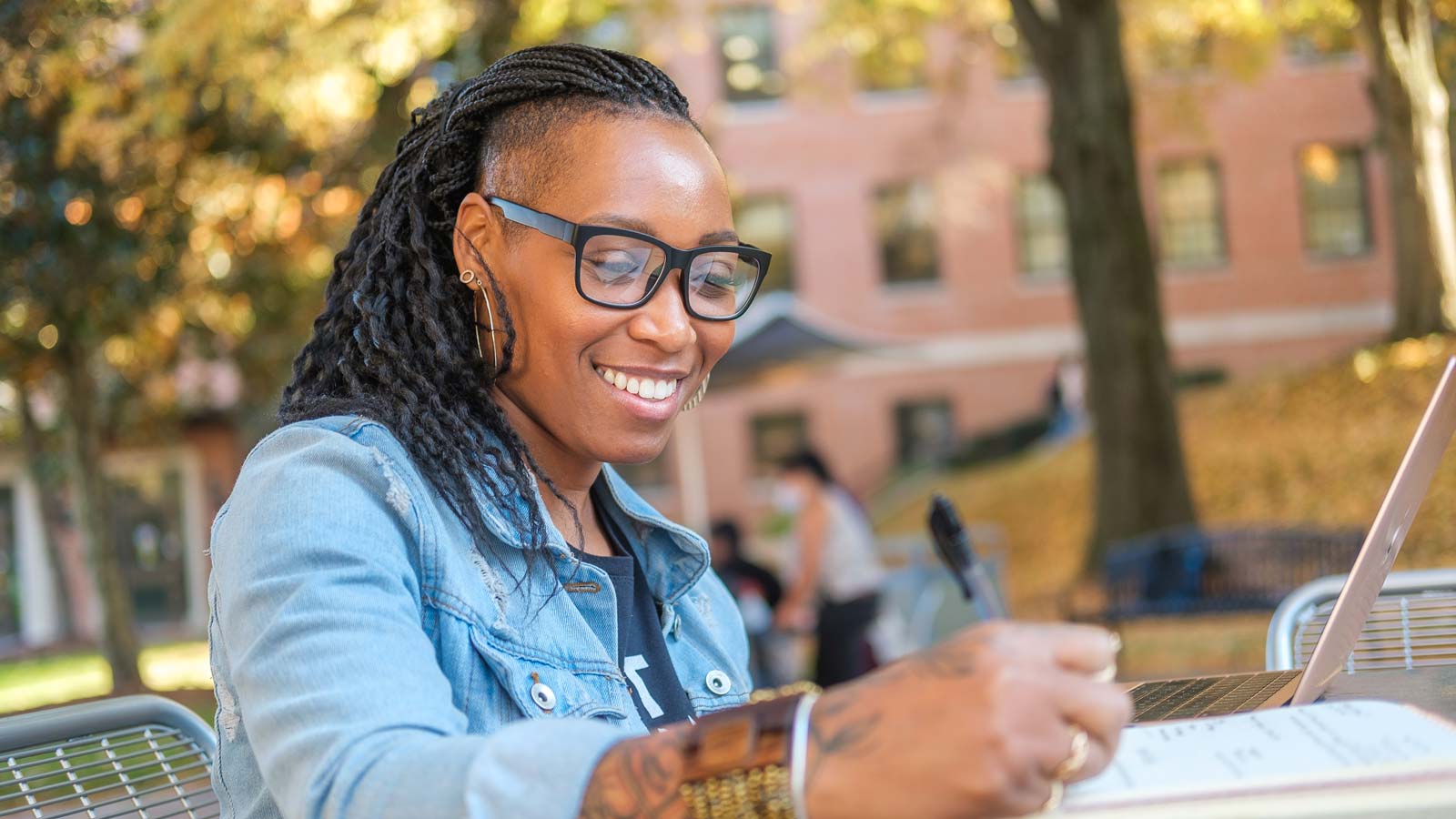person smiling, taking notes in front of a laptop