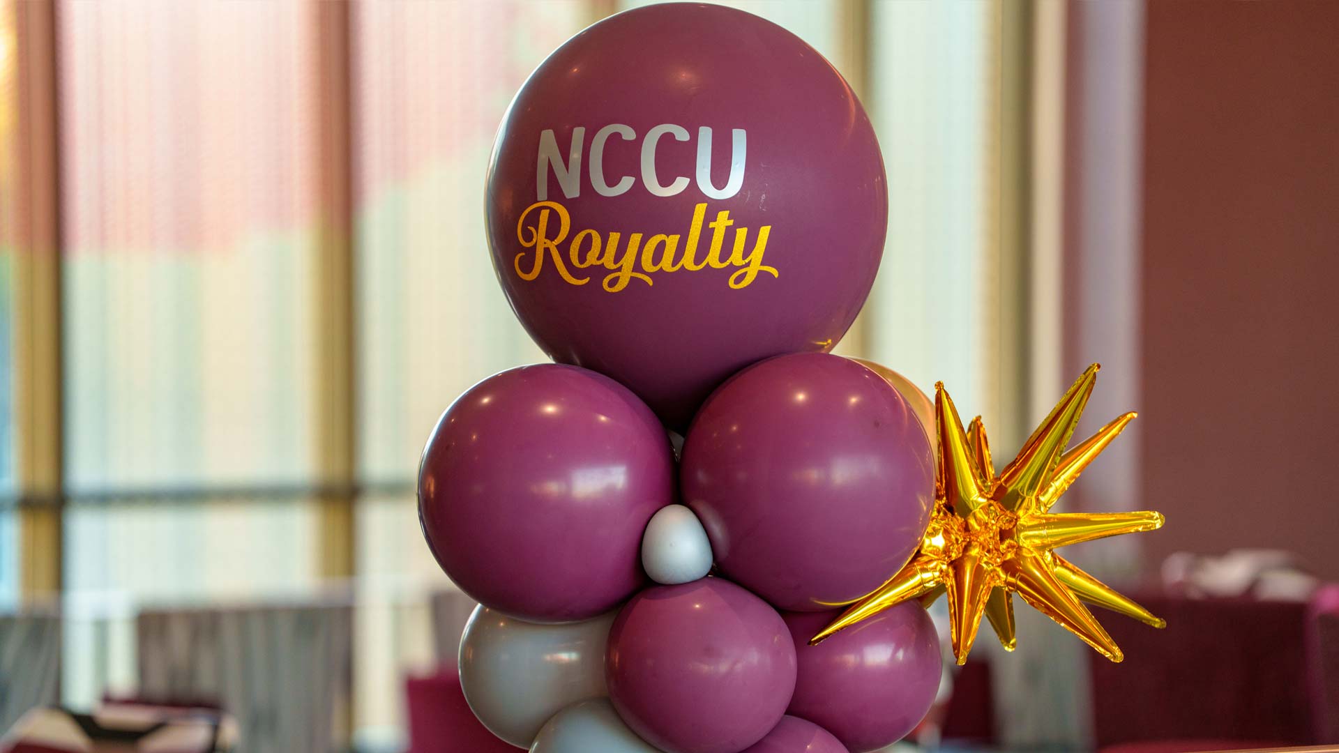 A balloon centerpiece feature maroon and white balloons with a large top balloon that reads "NCCU Royalty" in white and yellow text alongside a gold starfoil balloon accent.