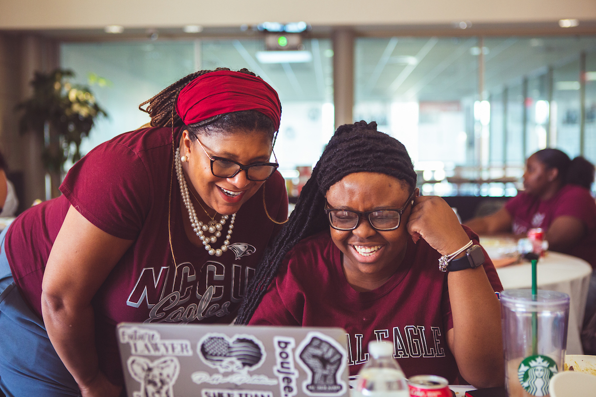 Two students looking at a laptop and smiling