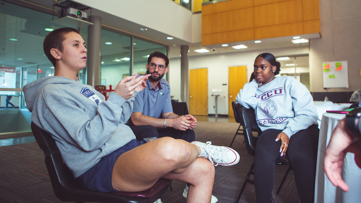 Three students sitting in chairs and having a discussion