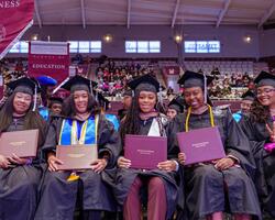 Graduates in caps and gowns holding diplomas, smiling at a ceremony.