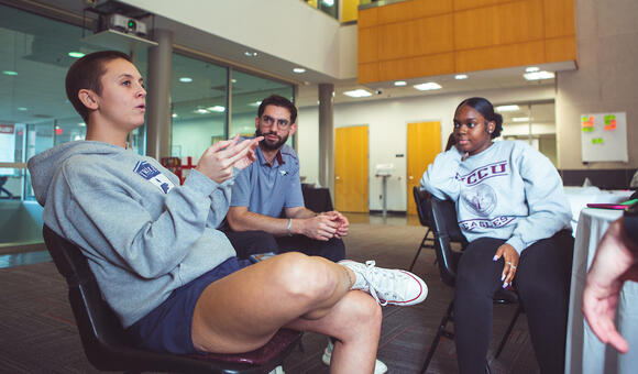 Three students sitting in chairs and having a discussion