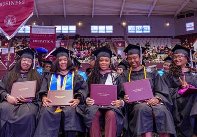 Graduates in caps and gowns holding diplomas, smiling at a ceremony.