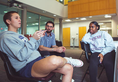 Three students sitting in chairs and having a discussion